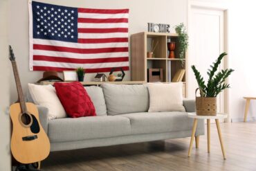 standard living room with a couch, a few pillows, an acoustic guitar, and a large American flag on the wall