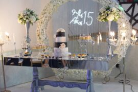 An elegant dessert table that has a cake, cupcakes, and other desserts on it as well as floral arrangements for a quince.