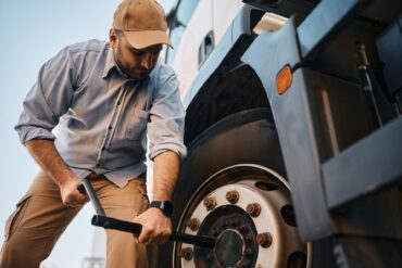 A young truck driver crouches beside his truck while changing a flat tire in order to get back on the road.