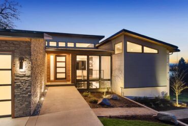 A modern style luxury home is illuminated from the inside at sunset so it looks like it's glowing against the dark blue sky.