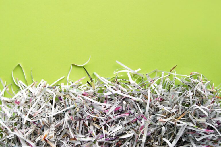 A large pile of shredded papers sits against a bright green background. The papers contain letters and colors.