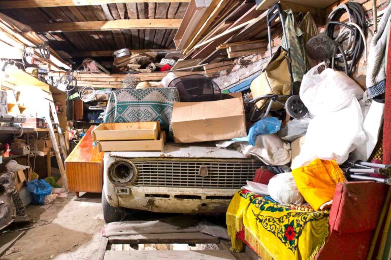 A close-up of the interior of a residential garage that's overflowing with tools, lumber, and an old car.