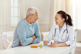 A caregiver sitting with a senior patient as they discuss treatment plans. There are two medications on the table.