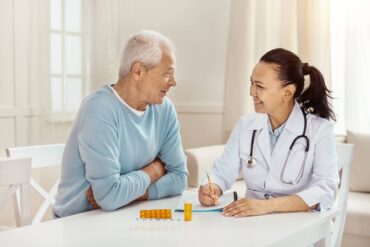 A caregiver sitting with a senior patient as they discuss treatment plans. There are two medications on the table.