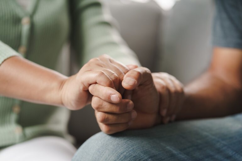 A close up shot of two people holding hands in an office setting. One person's hand is also on the other's arm.