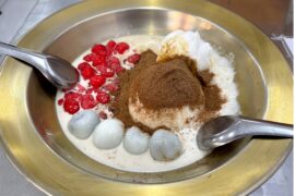 A Thai dessert dish consisting of mung bean, raspberries, sticky rice, and more with cocoa powder on top.