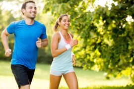 A man and a woman are going on a run outside. The sun is shining, and there is a tree near them.
