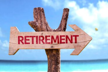 A wooden sign attached to a tree with the word retirement on it. There's a beach in the background.