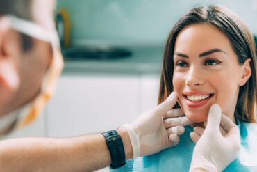 A woman looking at a person with a mask on and showing her teeth. The person with the mask on is touching her jaw.