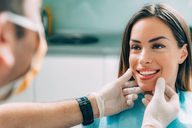 A woman looking at a person with a mask on and showing her teeth. The person with the mask on is touching her jaw.