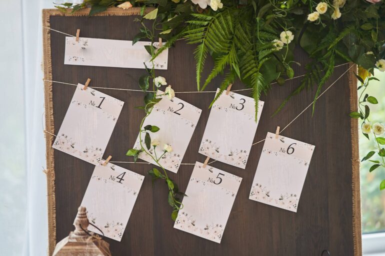A decorative board with pieces of paper hanging on a string. They have different table numbers for the wedding guests.