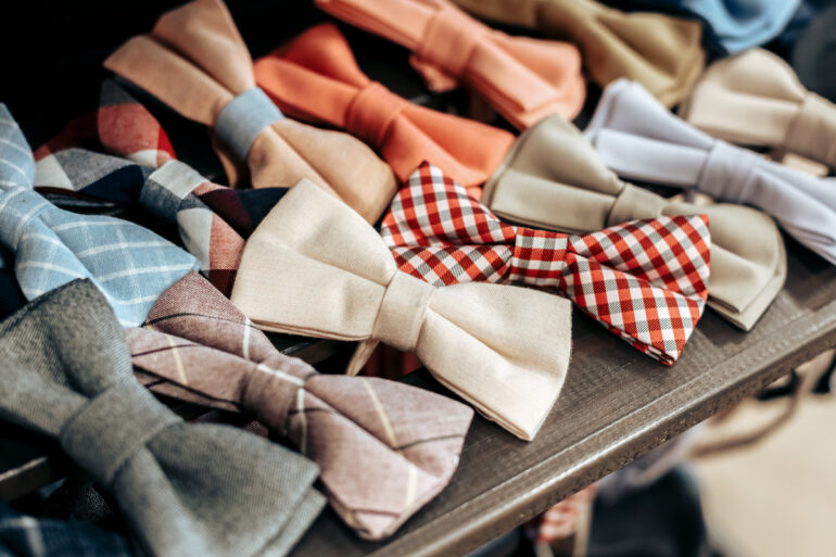 A close-up view of various solid-color and striped bowties arranged neatly at an angle on a brown wooden shelf.