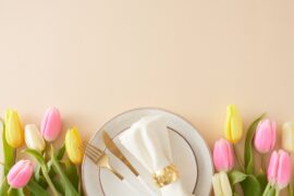 A gold fork, gold knife, and a white napkin wrapped in a gold cuff sit on a white plate with gold trim.