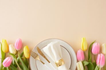 A gold fork, gold knife, and a white napkin wrapped in a gold cuff sit on a white plate with gold trim.