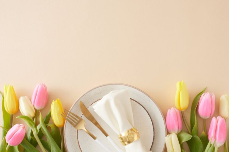 A gold fork, gold knife, and a white napkin wrapped in a gold cuff sit on a white plate with gold trim.