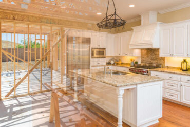 A kitchen with white cabinets and granite counter tops; wood framework aligns the back wall, exposing the outdoors.