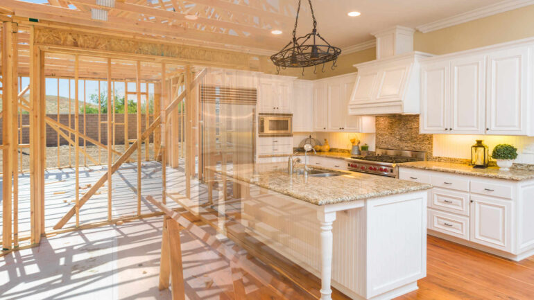 A kitchen with white cabinets and granite counter tops; wood framework aligns the back wall, exposing the outdoors.
