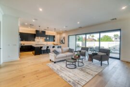 A home with an open floor plan contains an open kitchen, a white couch, two gray chairs, a gray rug, and large glass doors.