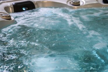 A close-up of the bubbling turquoise water of a large hot tub, with dials and lights along the side.