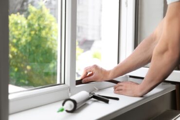 A close-up of a construction worker putting sealing foam tape on a window to stop water from entering the building.