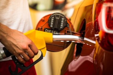 Close-up of a man inserting a nozzle into the fuel tank of his vehicle. The back of the gas cap reads "diesel."