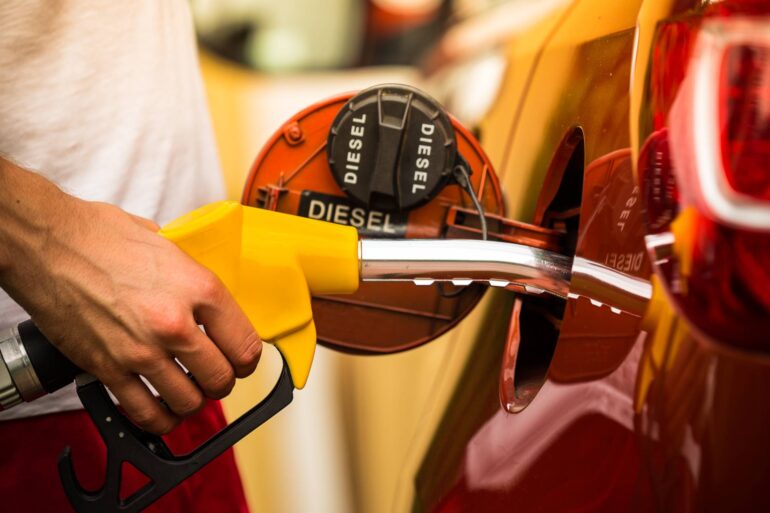 Close-up of a man inserting a nozzle into the fuel tank of his vehicle. The back of the gas cap reads "diesel."