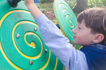A young boy interacts with a piece of sensory playground equipment designed to improve fine motor skills.