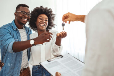 A young black couple are getting keys to a new property. They're both smiling and laughing.