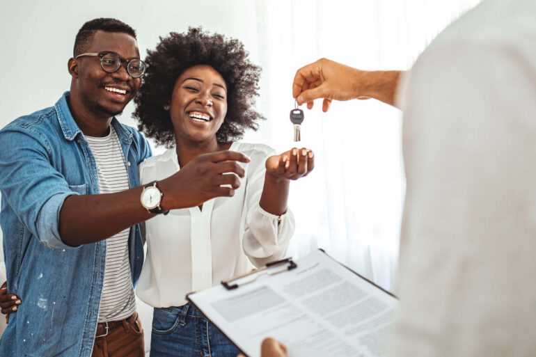 A young black couple are getting keys to a new property. They're both smiling and laughing.