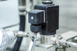 A black plastic valve sits on top of silver poles. A white plastic tube comes out of the black plastic valve.