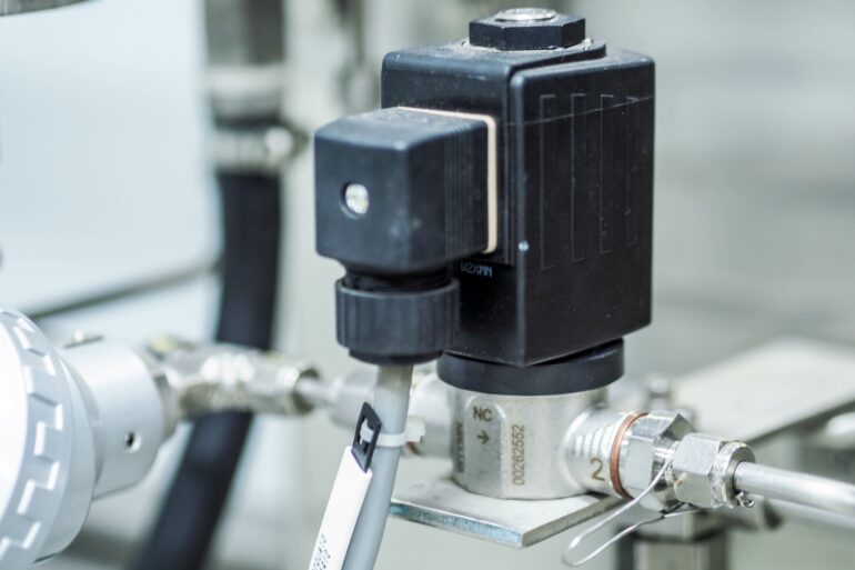 A black plastic valve sits on top of silver poles. A white plastic tube comes out of the black plastic valve.
