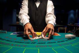 A dealer at a blackjack table shuffles a deck of cards with rows of playing chips of different colors in front of them.