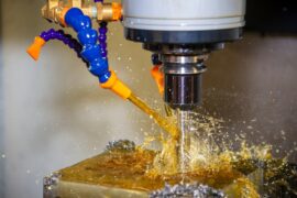A CNC milling drill being sprayed with industrial lubricant. The lubricant is light brown and the sprayer is blue.