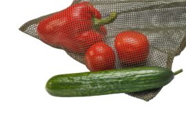 A green mesh laundry bag being used for food. There's a red pepper and tomatoes inside the bag and a cucumber outside of it.