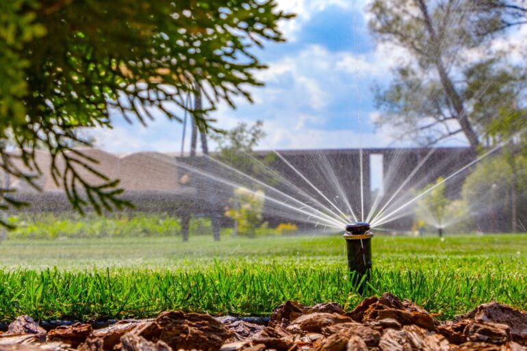 An up close commercial property irrigation sprinkler head. The sprinkler head is on and water is spraying on the lawn.