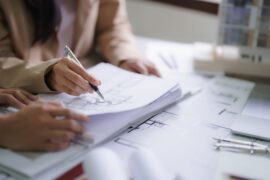 Close up of people's hands as they hold and point at various interior design blueprints. One hand holds a pen.