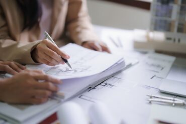 Close up of people's hands as they hold and point at various interior design blueprints. One hand holds a pen.