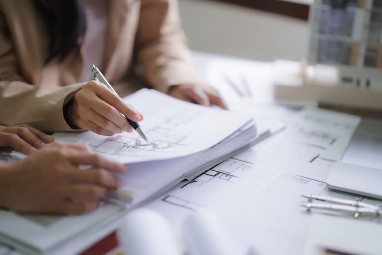 Close up of people's hands as they hold and point at various interior design blueprints. One hand holds a pen.