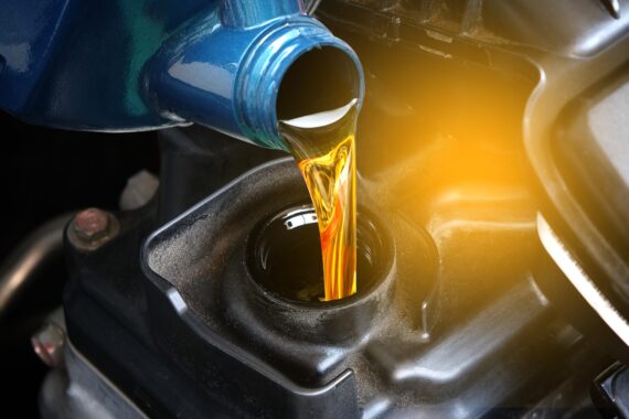 A close-up view shows a thick, yellow liquid from a blue bottle being poured into an opening on an engine.