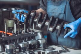 A mechanic wearing blue latex gloves as they hold onto an engine block to prepare it for cleaning. Tools are on the table.