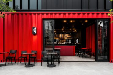 A red shipping container business is open. There are seats and tables outside, and the check-out station is inside.