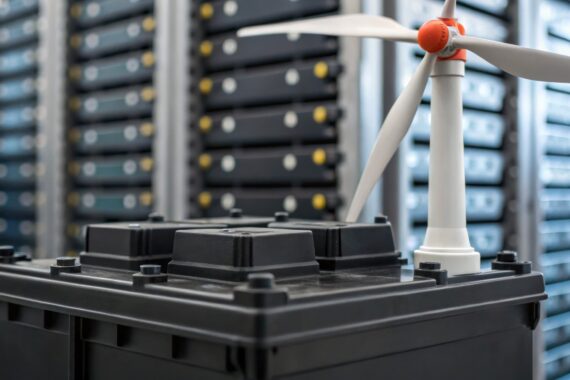 Near several tall stacks of servers inside a data center, a small model of a white wind turbine sits atop a large battery.
