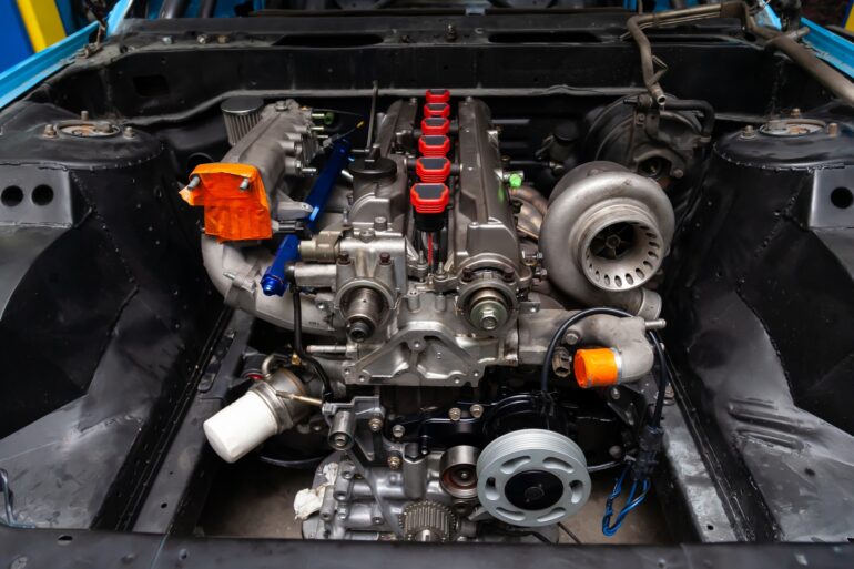 A car's hood open with a supercharger engine sitting in the center. There are six red gaskets in the middle of the charger.