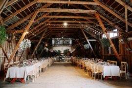 The interior of a barn with long decorated tables and flowers and string lights hanging from the ceiling.