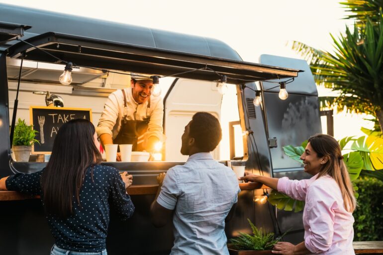 Two women and one man stand at the counter of a mobile drink shop. A man stands at the counter inside the truck.