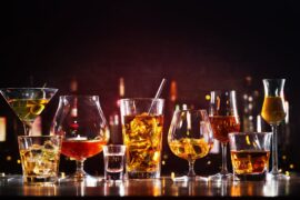 An assortment of bar glasses with beverages in them, including martinis, champagne, mixed cocktails, and garnishments.