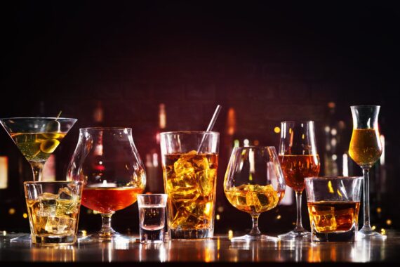 An assortment of bar glasses with beverages in them, including martinis, champagne, mixed cocktails, and garnishments.