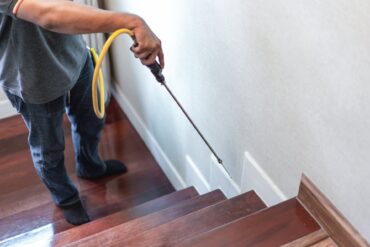 A pest control company is spraying the destructive chemical liquid onto the side of the wooden staircase.