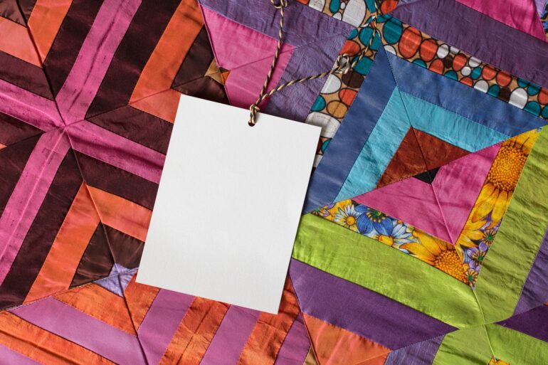 A close-up on a handmade quilt made of bright colors and patterns. A blank greeting card is attached.