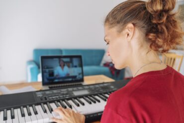 A woman with curly hair in a ponytail sits in front of a keyboard with a tablet propped up behind it.